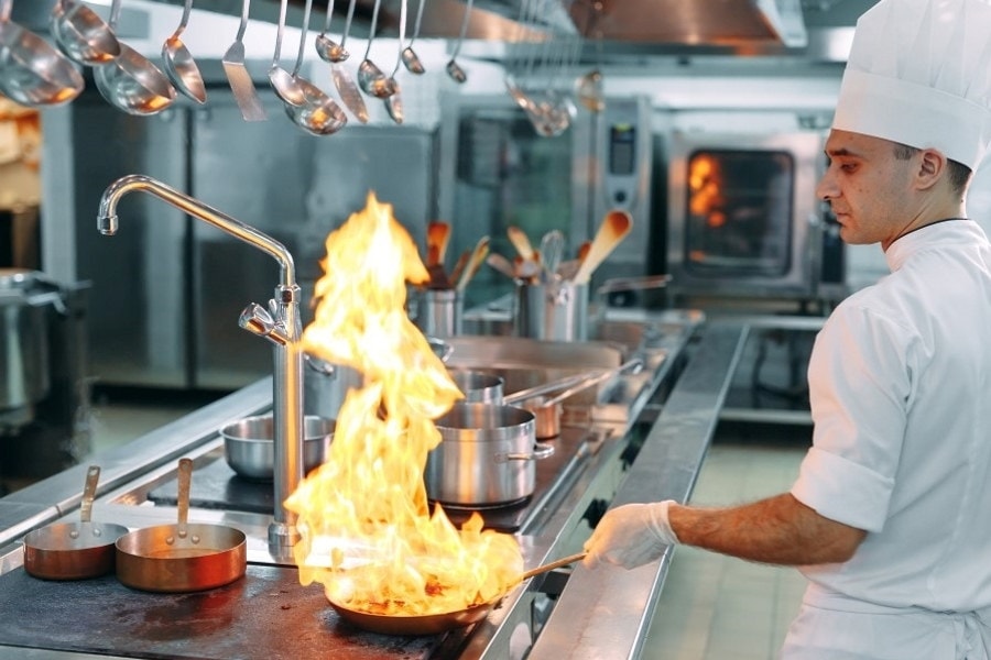 Mann på kjøkken som flamberer mat. Foto.