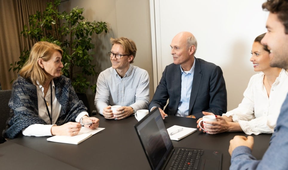 Mennesker som sitter rundt et bord og konverserer. Foto.